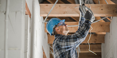 Professional Electrician in His 40s Installing Ceiling Light Point Inside Newly Developed Concrete Brick House with Wooden Beams Roof Structure.